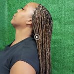 A woman with long braids on her head, wearing a colorful traditional dress and smiling brightly.